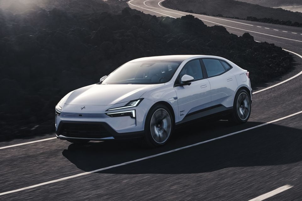 A white Polestar 4 SUV coupe driving on a winding road, seen from the front-side