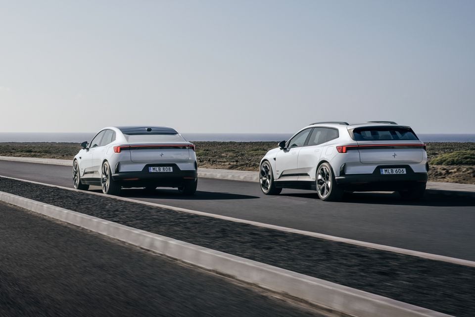 Two white Polestar electric vehicles seen from the rear driving along a coastal road, showing a sedan and an SUV body style side by side