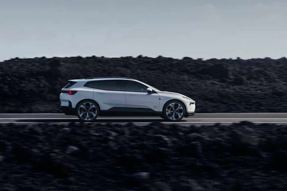 A white Polestar 4 SUV seen from the side while driving on a road, with a rocky landscape in the background