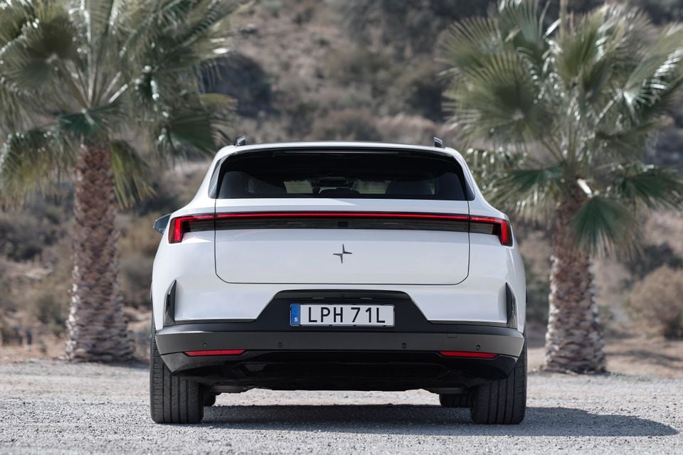 A white 2027 Polestar 4 SUV parked on gravel between two palm trees, seen from the rear