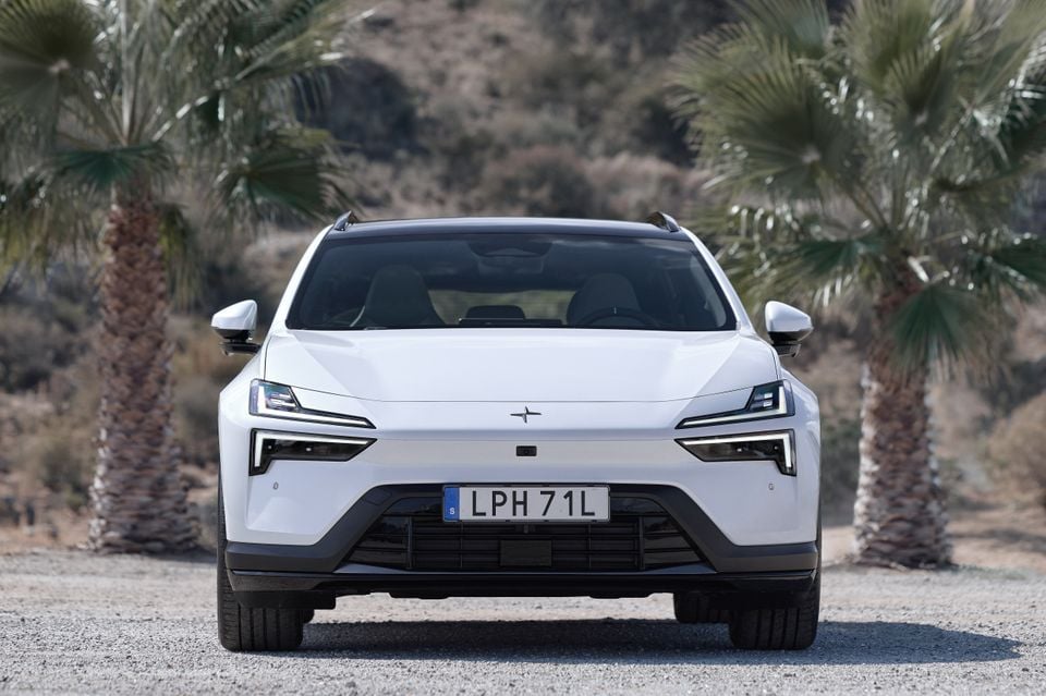 A white 2027 Polestar 4 SUV parked on gravel between two palm trees, seen from the front