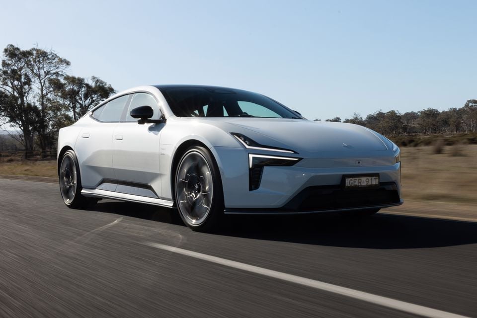 A silver 2027 Polestar 5 Performance sedan driving on a country road, seen from the front three-quarter angle