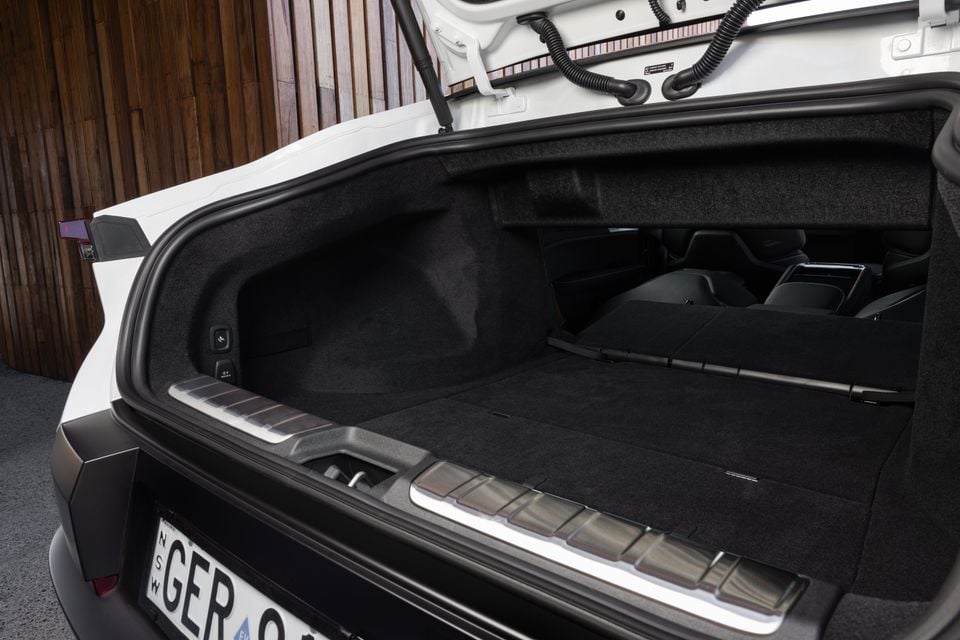 Open boot of a white 2027 Polestar 5 Performance with the rear seats folded flat, extending the carpeted load floor into the cabin