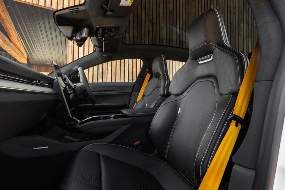 Bancos dianteiros esportivos pretos com cintos de segurança amarelos dentro do 2027 Polestar 5 Performance, vistos pela porta do passageiro aberta, com volante e painel