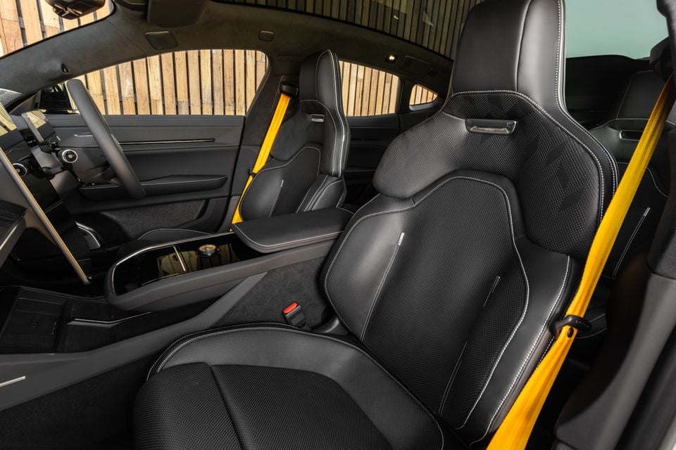 Black leather sports front seats with yellow seatbelts and the centre console inside the 2027 Polestar 5 Performance, seen through the passenger door