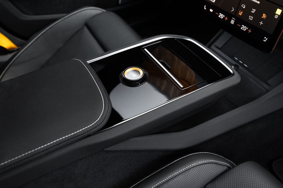 Centre console of the 2027 Polestar 5 Performance with a gloss black finish, gold-ringed rotary dial, covered storage and touchscreen climate controls