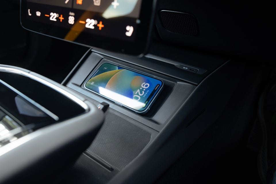 A smartphone charging on the wireless charging pad in the centre console of a 2027 Polestar 5, below the touchscreen showing climate controls.