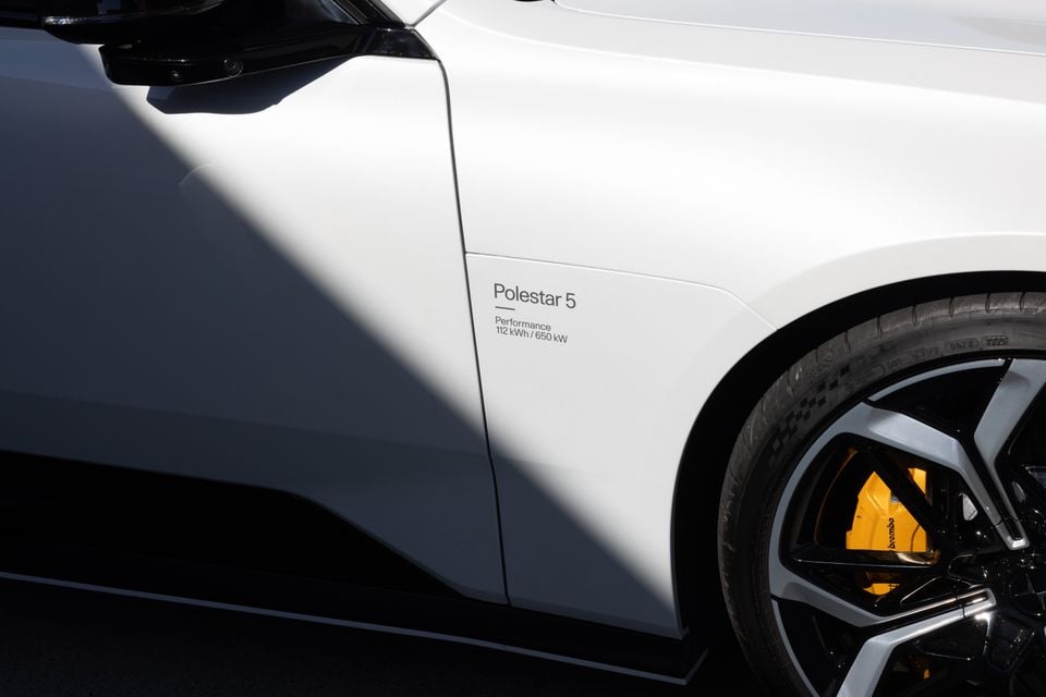 Close-up of a white 2027 Polestar 5 Performance front guard showing its model decal, side mirror and wheel with yellow Brembo brake caliper