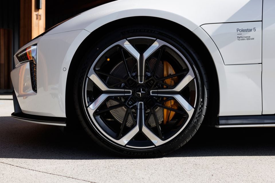 Close-up of the front wheel of a white 2027 Polestar 5 Performance, showing its black and silver alloy rim, gold brake caliper and Michelin tyre