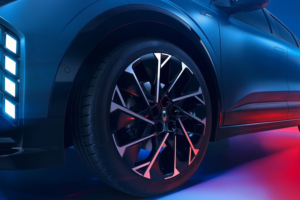 Close-up of the front wheel of a blue 2027 Renault Megane E-Tech Esprit Alpine, showing its black and silver alloy rim and illuminated front lights