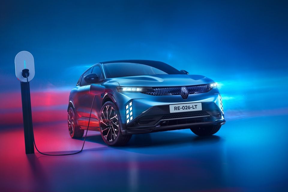 A blue 2027 Renault Megane E-Tech Esprit Alpine plugged into a wall charger in a studio, seen from the front three-quarter angle
