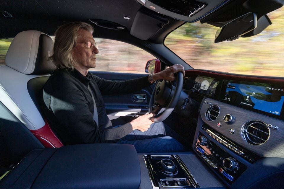 A man driving the 2027 Rolls-Royce Spectre, seen from the passenger side showing the steering wheel, digital dashboard screens and centre console