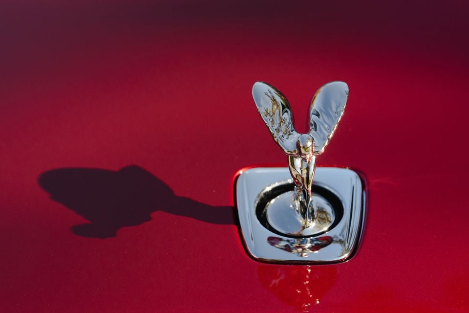 Close-up of the chrome Spirit of Ecstasy mascot on the red bonnet of a 2027 Rolls-Royce Spectre, casting a shadow across the paint.