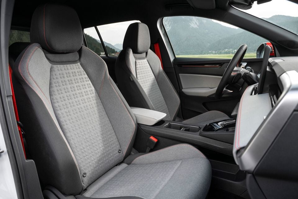 Interior view of the 2027 Skoda Epiq First Edition showing front seats with grey patterned fabric upholstery and red contrast stitching, centre console, and steering wheel with mountains visible through the windows.