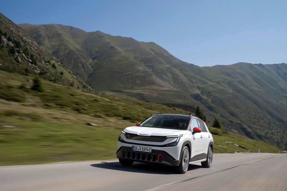 A white Skoda Epiq SUV driving along a mountain road, seen from the front side