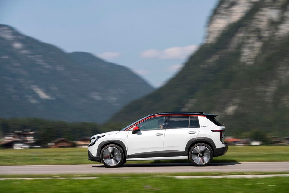 A white Skoda Epiq SUV seen from the side, driving along a road with mountains in the background
