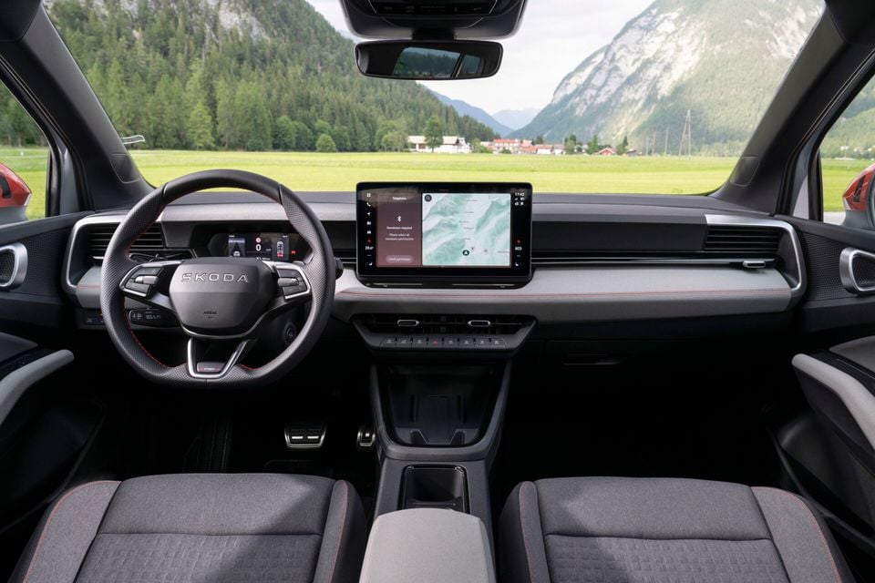 Interior of a Skoda Epiq showing the dashboard, steering wheel with Skoda branding, large central touchscreen displaying a navigation map, and front seats with red stitching detail