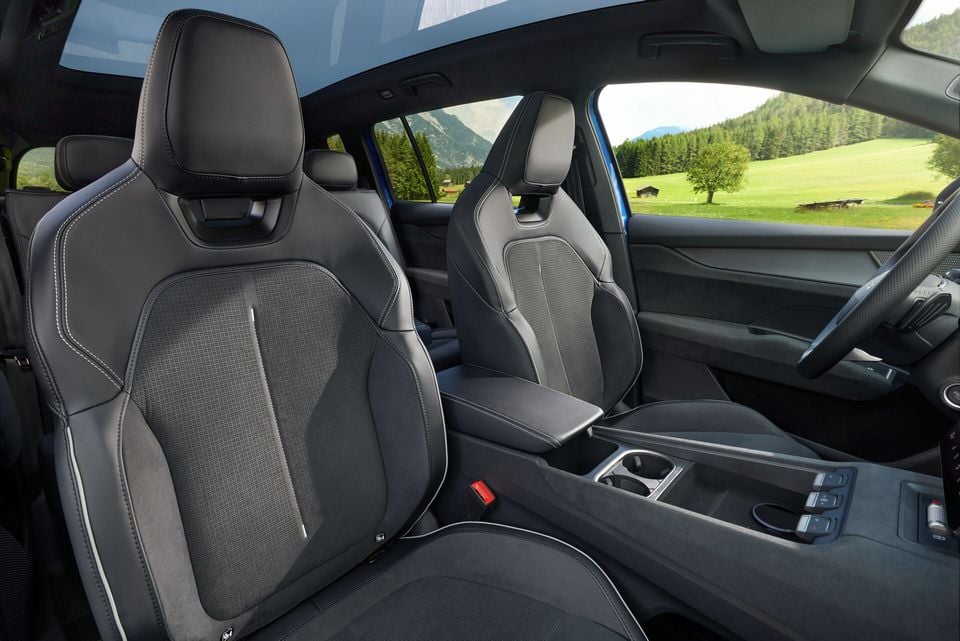 Interior view of a 2027 Skoda Elroq Sportline showing the front seats with dark fabric and leather upholstery, centre console with cup holders, and a scenic mountain backdrop through the windows.