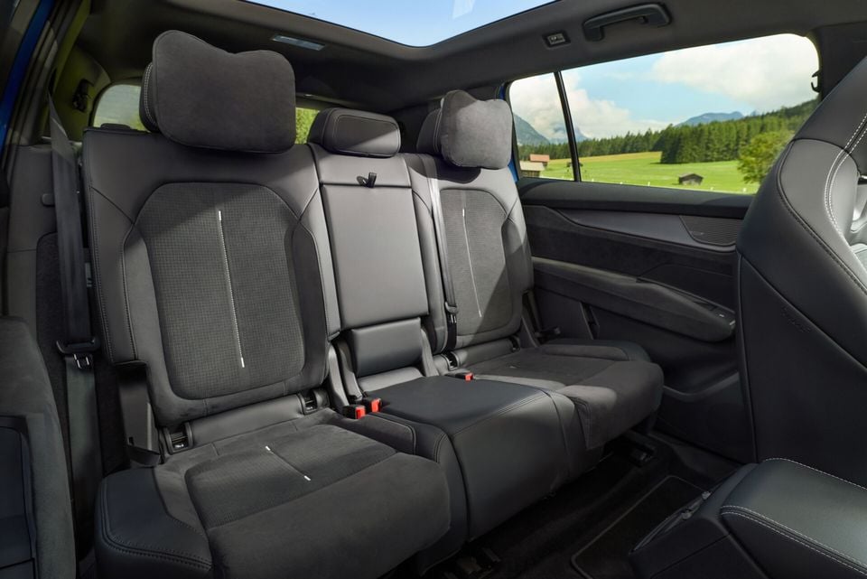 Rear passenger seats of a Skoda Elroq SUV showing dark fabric upholstery, three headrests, and a panoramic sunroof, with a scenic mountain view through the window