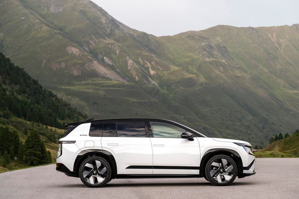 A white Skoda Peaq SUV seen from the side, parked on a road with green mountains in the background