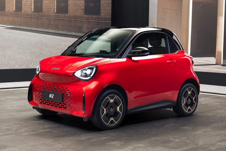 A red 2027 Smart #2 two-door city car with a black roof, seen from the front three-quarter angle parked on a concrete floor