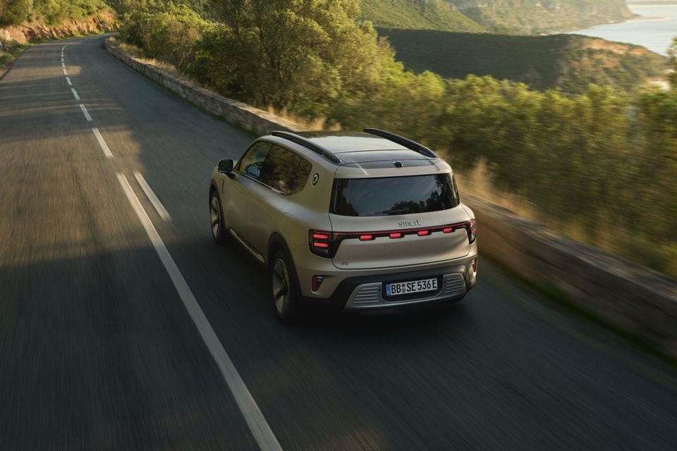 A beige Smart #5 SUV seen from the rear while driving along a winding coastal road