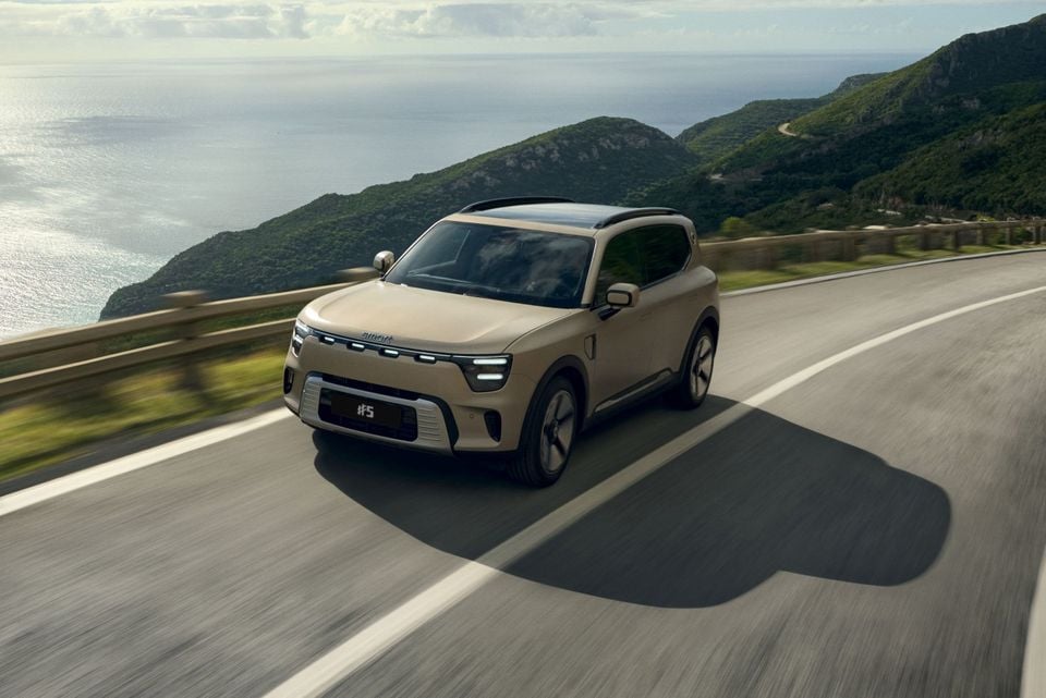 A beige Smart #5 SUV driving along a coastal mountain road, seen from the front-left