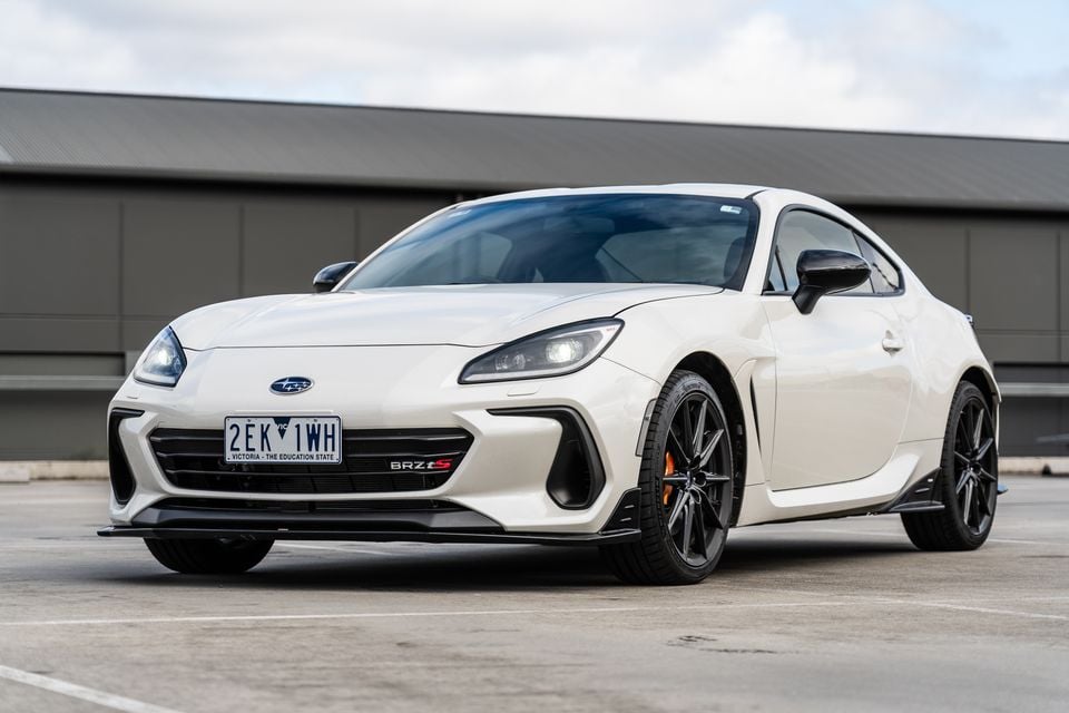 A white Subaru BRZ tS coupe seen from the front three-quarter angle in a car park, featuring a black front splitter, black alloy wheels, and orange brake callipers