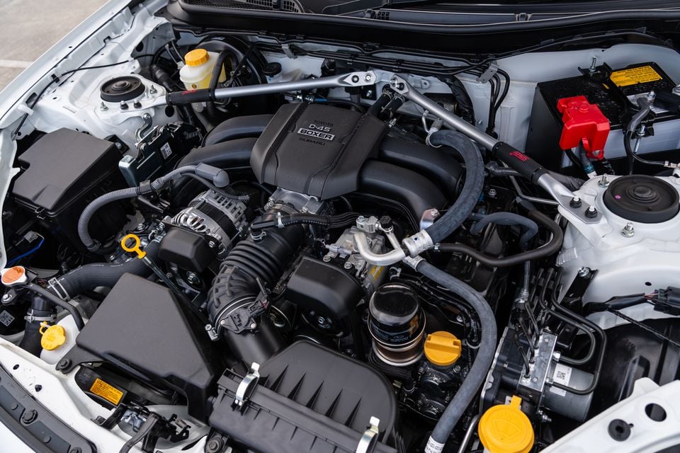 The Toyota D-4S Boxer engine bay of a Subaru BRZ, showing the flat-four engine, strut brace, and surrounding components with the bonnet open.
