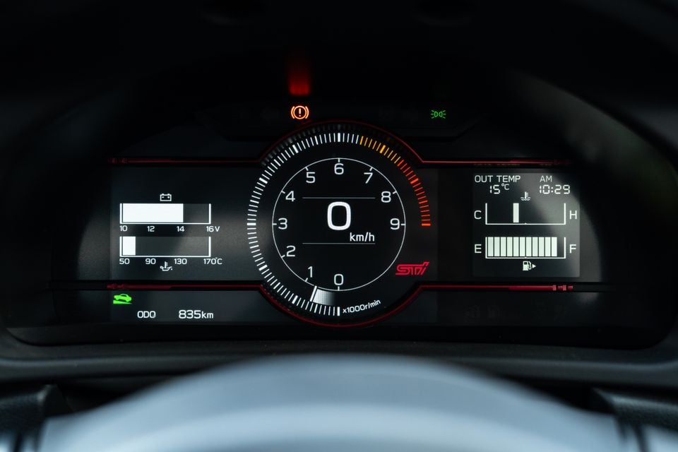Subaru BRZ tS digital instrument cluster showing a central tachometer with STI branding, speedometer reading zero, voltage and oil temperature gauges on the left, and fuel level and coolant temperature on the right