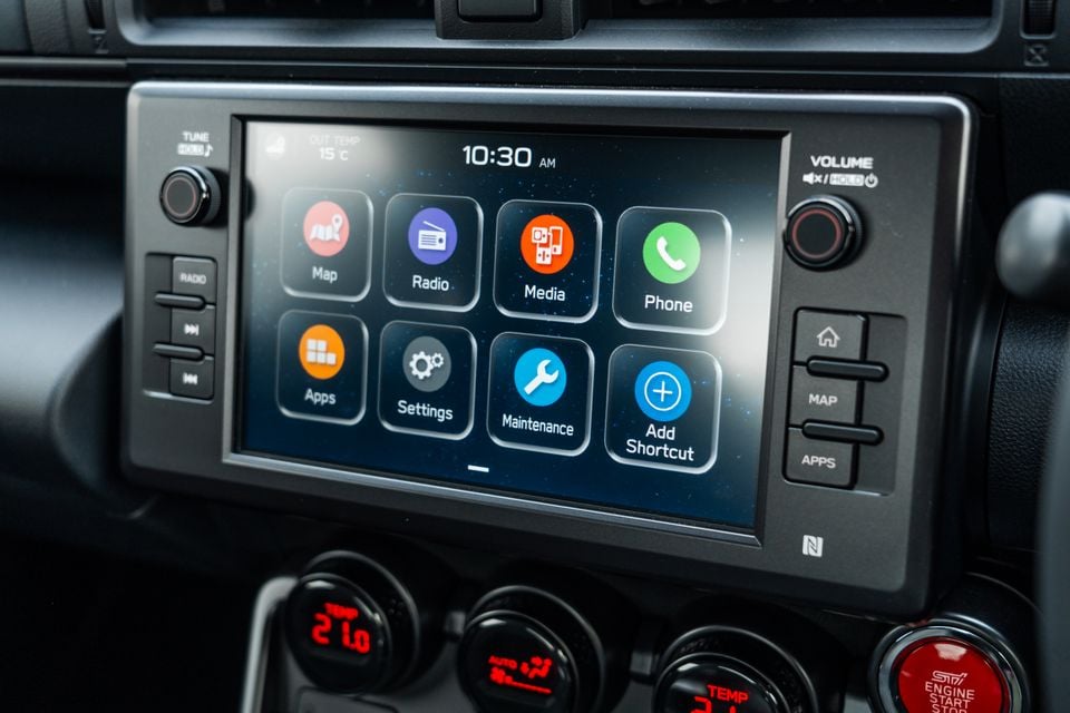 Close-up of the infotainment touchscreen in a Subaru BRZ tS, showing the home menu with Map, Radio, Media, Phone, Apps, Settings, Maintenance and Add Shortcut icons, alongside physical controls and climate dials below.