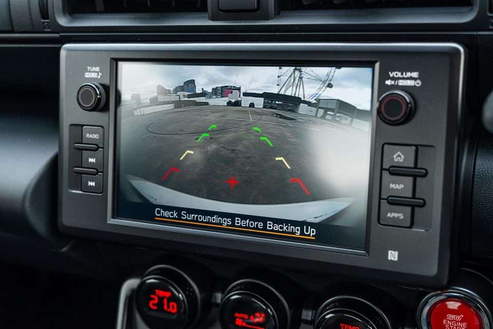 Subaru BRZ tS infotainment screen displaying the reversing camera view with parking guidelines and a 'Check Surroundings Before Backing Up' warning message
