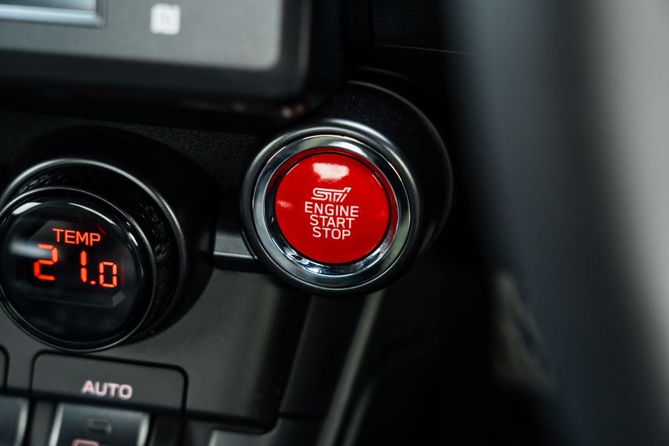Close-up of the red STI-branded engine start/stop button and climate control panel inside a Subaru BRZ tS
