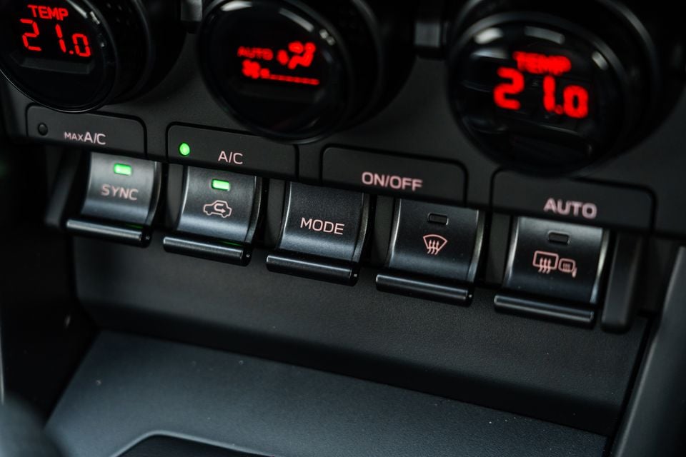 Close-up of the dual-zone climate control panel in a Subaru BRZ, showing sync, A/C, mode, and rear demister buttons with red digital temperature displays set to 21.0 degrees