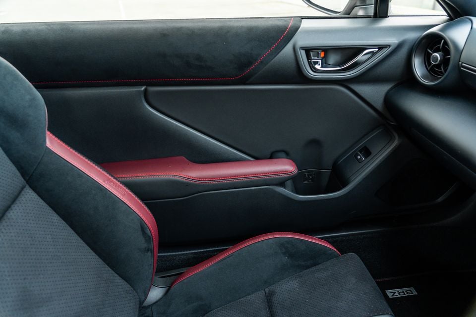 Interior of a Subaru BRZ showing the passenger door panel and front seat, with black alcantara upholstery and red leather accents with red stitching throughout