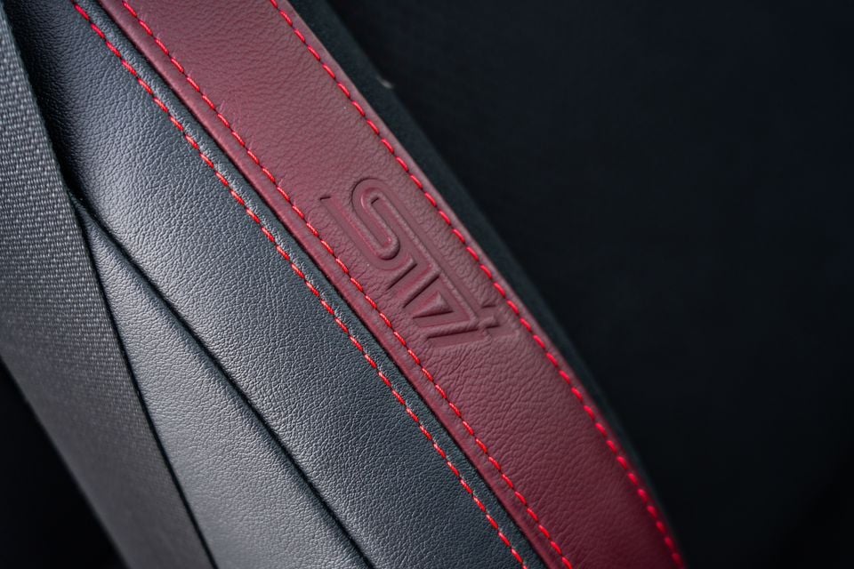 Close-up of the leather seat bolster in a Subaru BRZ tS, showing dark red upholstery with red contrast stitching and an embossed tS logo