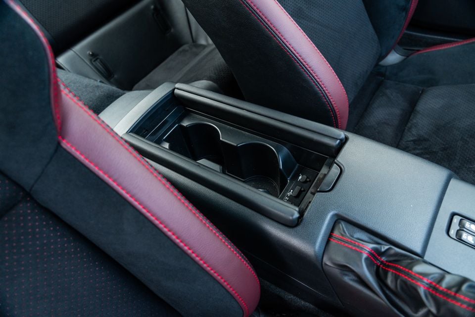 Interior centre console of a Subaru BRZ tS showing dual cup holders with a sliding cover and red-stitched black upholstery trim on the seats and armrest