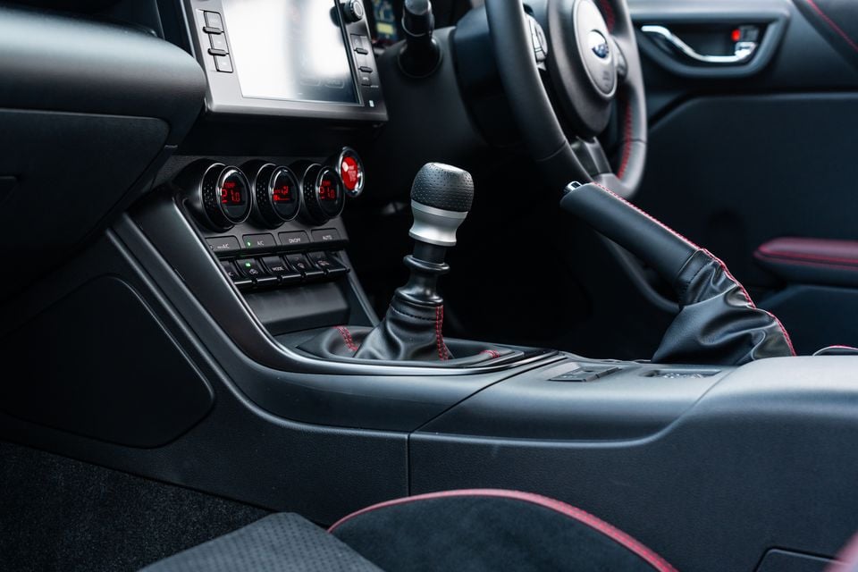 Interior of a Subaru BRZ tS showing the manual gear shifter with red stitching, climate control dials and steering wheel