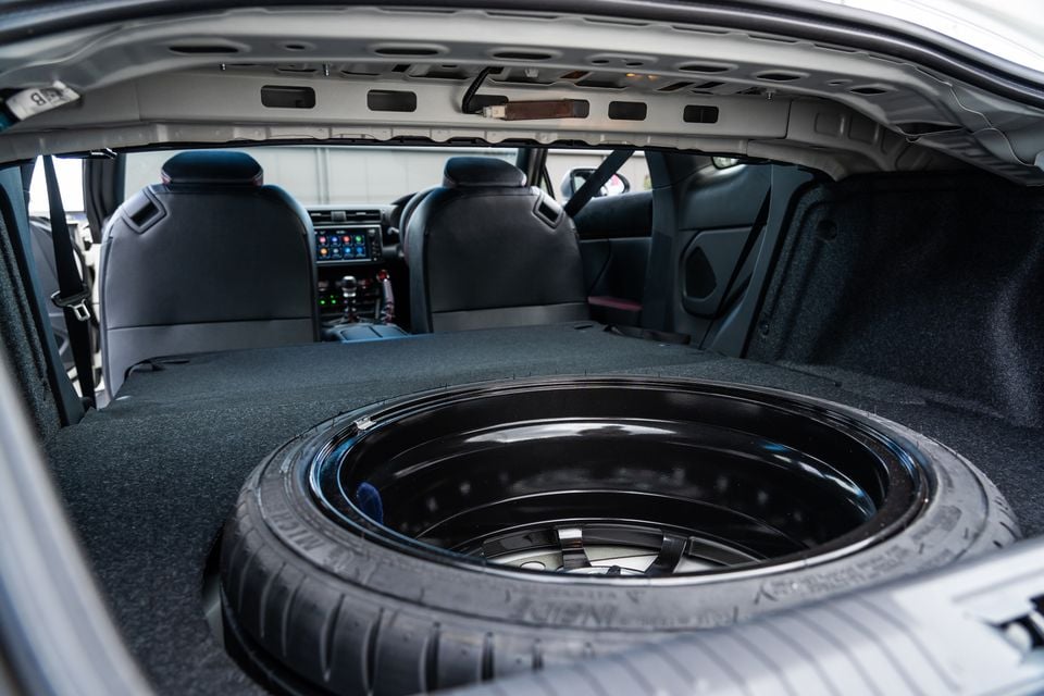 The open boot of a Subaru BRZ showing a spare wheel stored in the boot floor, with rear seats and infotainment screen visible in the background.