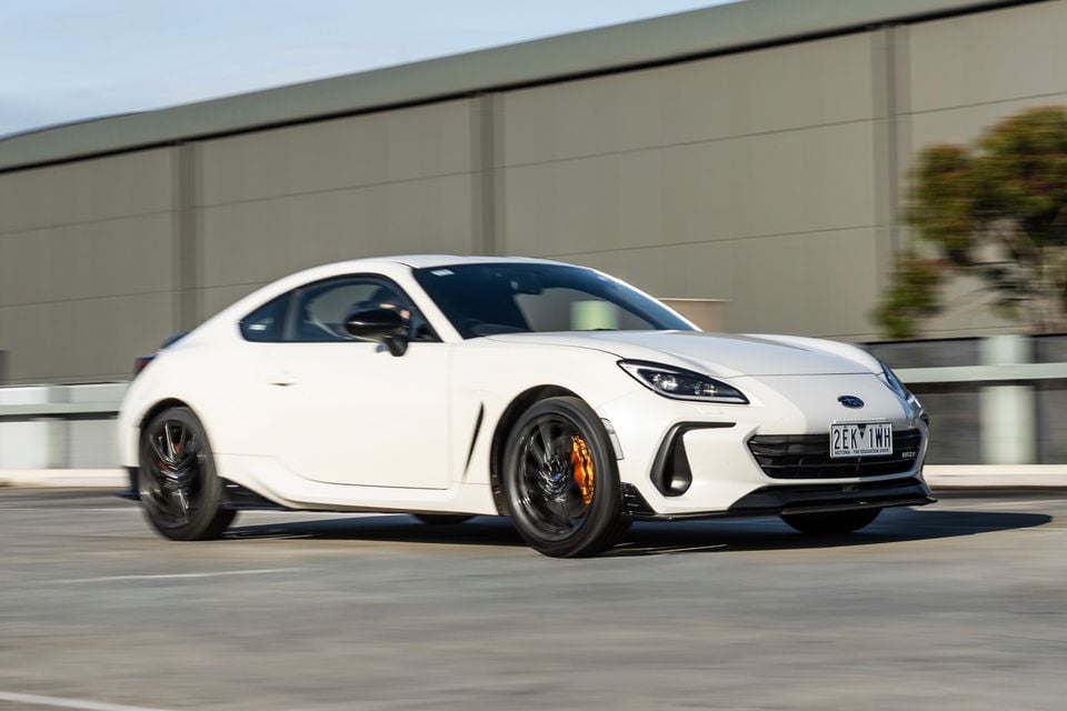 A white Subaru BRZ tS coupe driving on a road, seen from the front-side, with black wheels and gold brake calipers visible