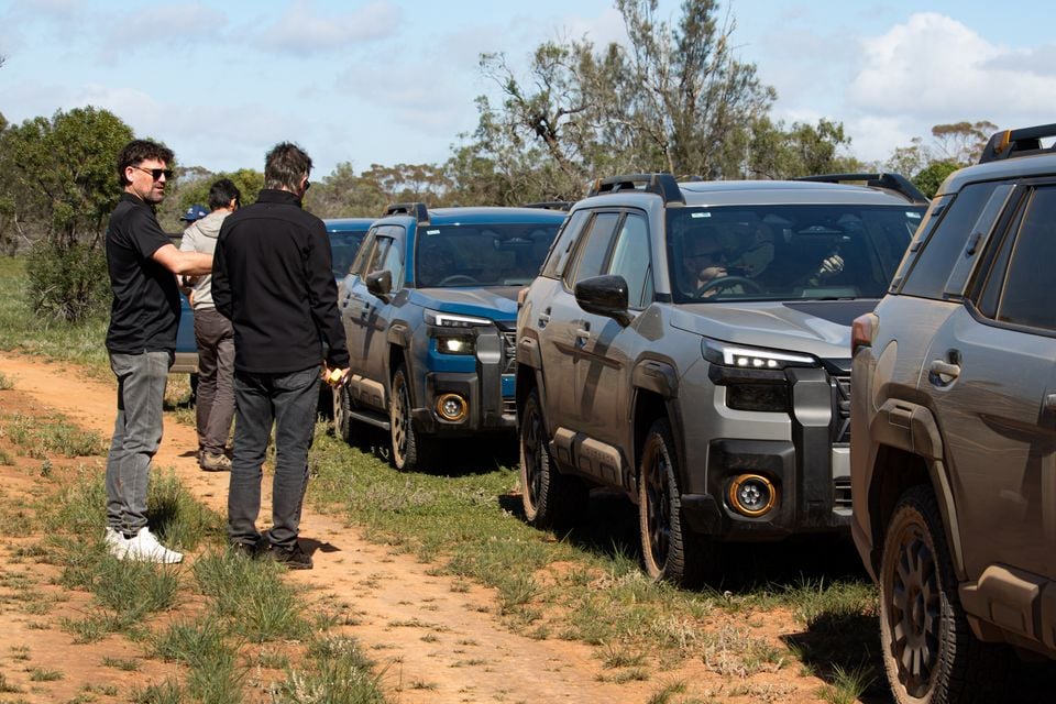Multiple Subaru Outback Wilderness SUVs lined up on a dirt track in the Australian bush during a media launch event, with several people standing alongside the vehicles