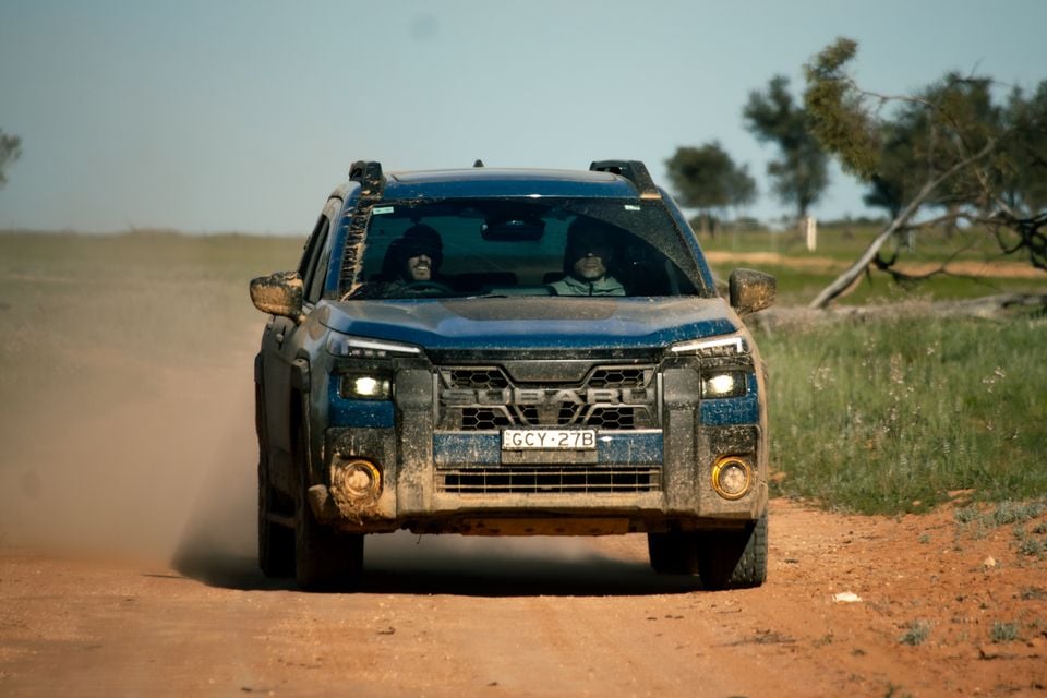 A muddy blue Subaru ute driving towards the camera on a dusty outback dirt road, seen from the front