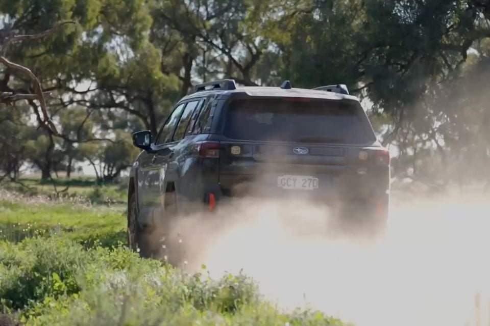 A Subaru Outback Wilderness SUV seen from the rear, kicking up dust on a dirt track surrounded by Australian bush