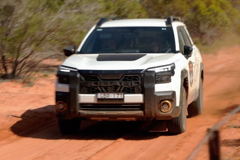A white Subaru Outback Wilderness driving on a red dirt track in the Australian outback, seen from the front