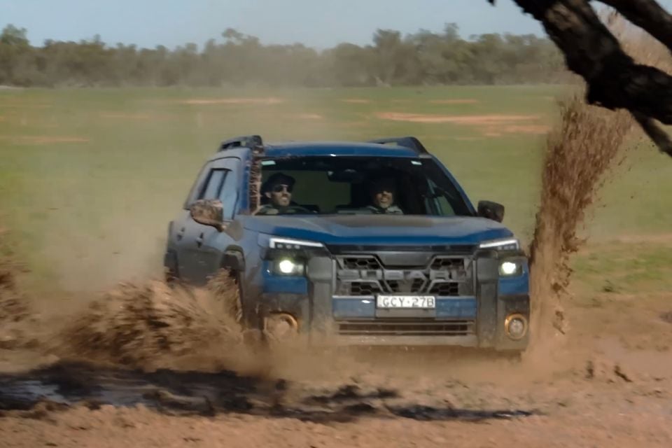 A blue Subaru Outback Wilderness driving through mud and dirt in an outback Australian landscape, seen from the front