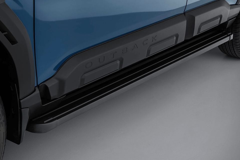 Close-up of the side sill and running boards on a blue Subaru Outback Wilderness, showing the embossed 'Outback' lettering on the body cladding