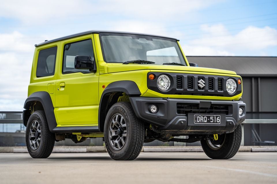 A yellow-green Suzuki Jimny small 4WD seen from the front-side angle in an outdoor setting