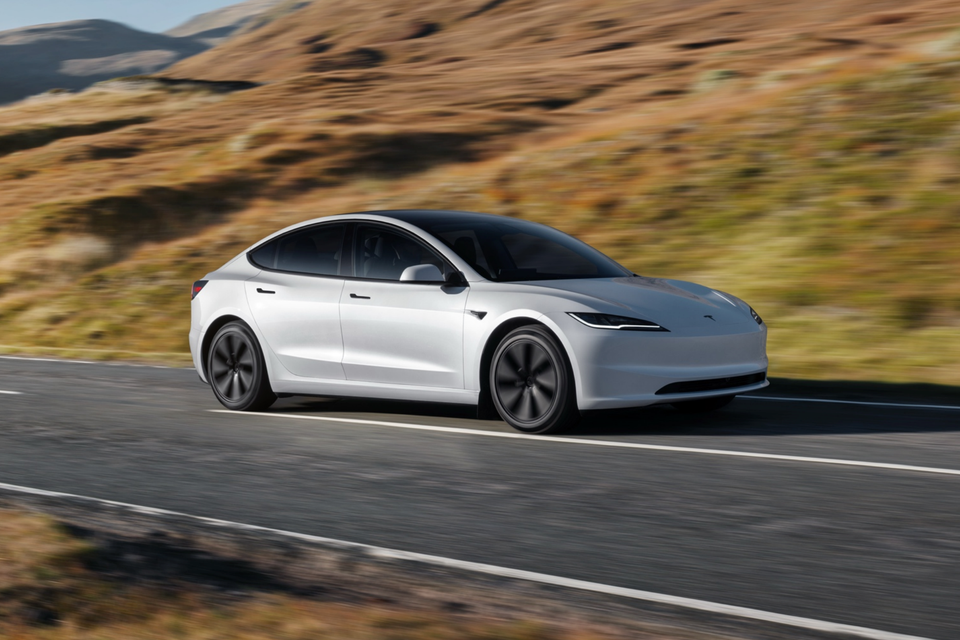 A white Tesla Model 3 sedan driving on a rural road with hills in the background