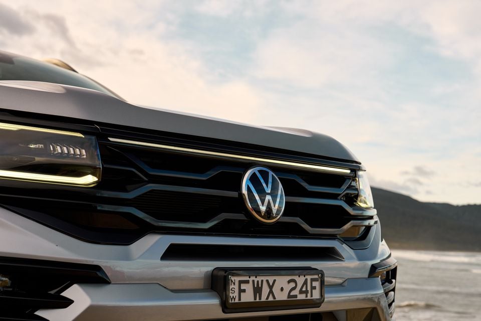 Close-up of the front grille and VW badge on a Volkswagen Amarok, with LED headlights and an NSW number plate visible, parked near a coastal backdrop.