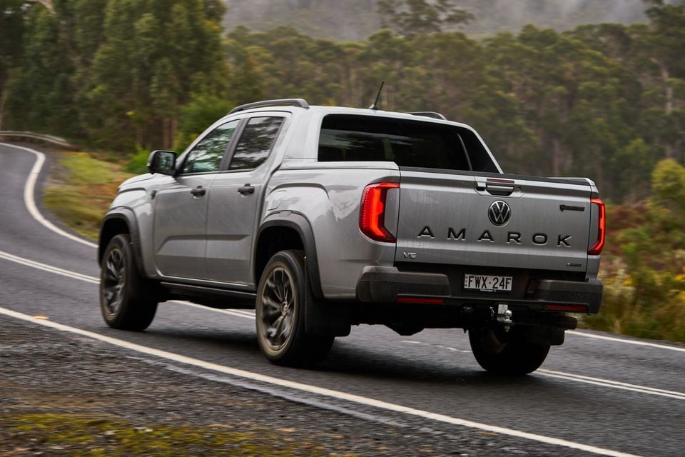 A silver Volkswagen Amarok V6 dual-cab ute seen from the rear while driving on a winding road surrounded by misty forest